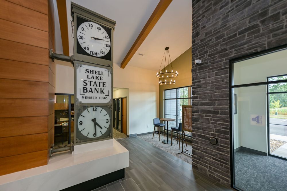 Shell Lake State Bank lobby featuring a vintage double-faced clock, wood accents, stone wall, and modern chandelier.