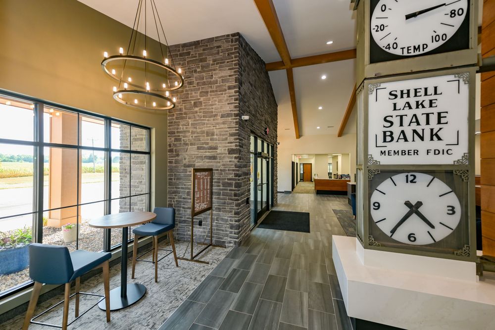 Modern bank lobby with Shell Lake State Bank clock, brick fireplace, pendant lights, and wood floors.