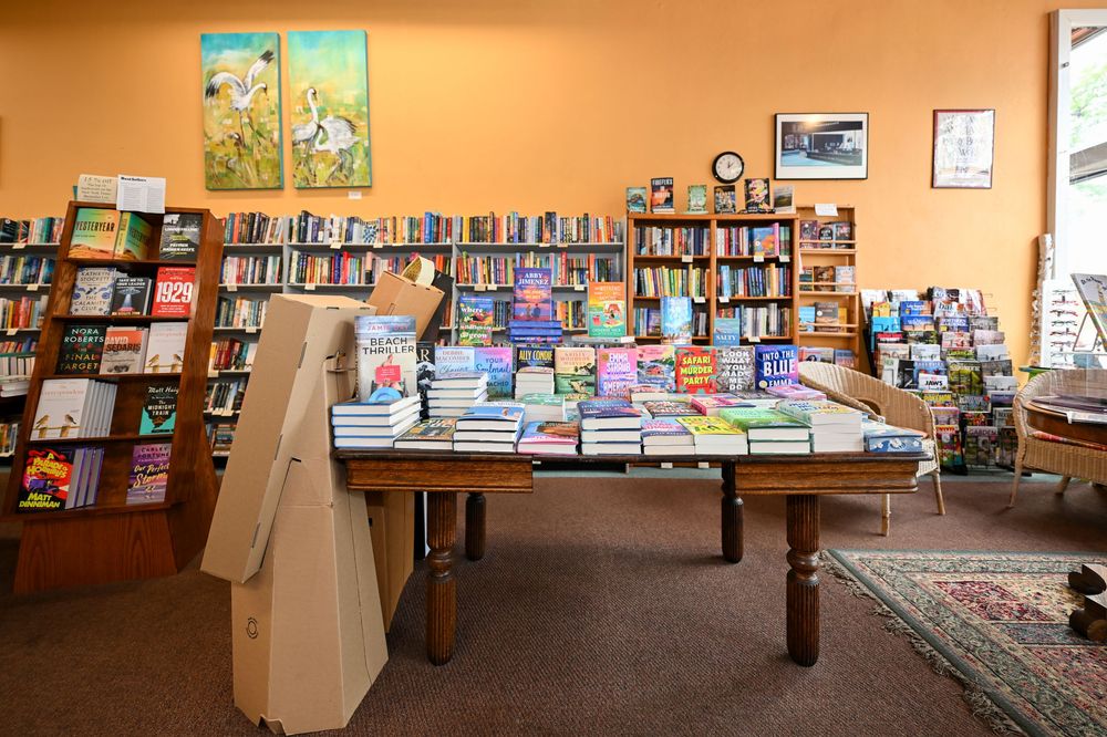 Cozy independent bookstore interior with wooden tables displaying colorful books and floor-to-ceiling shelves along orange walls.
