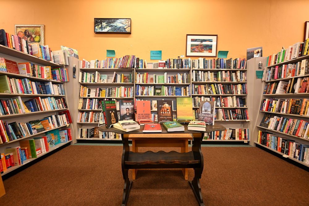 Cozy bookstore interior with wooden table display surrounded by tall shelves filled with colorful books on orange walls.