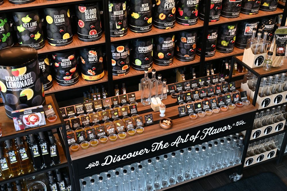 A retail display shelf featuring artisan hot sauces, seasonings, and flavored beverages with a Discover The Art of Flavor sign.
