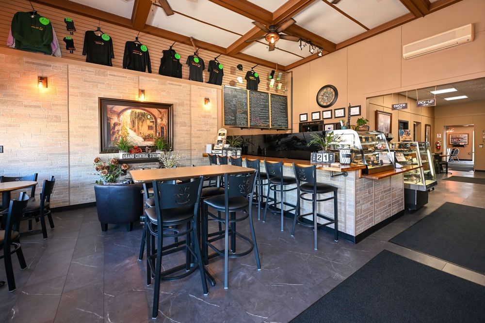 Cozy coffee shop interior with high bar seating, chalkboard menu, brick walls, and a well-stocked espresso bar counter.