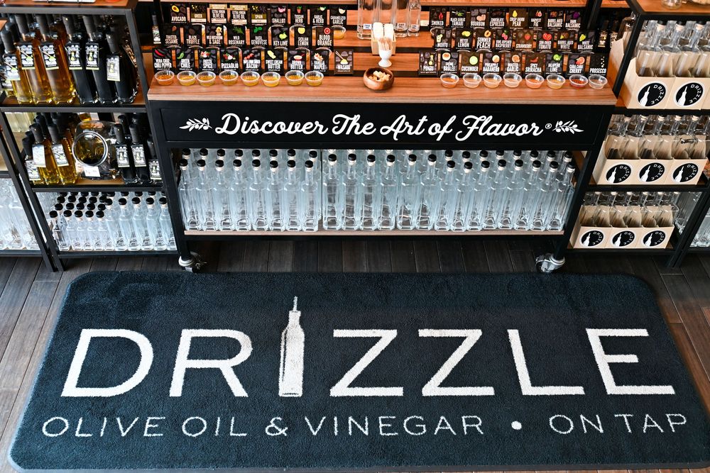 Drizzle Olive Oil & Vinegar On Tap store floor mat with bar display and Discover The Art of Flavor sign.