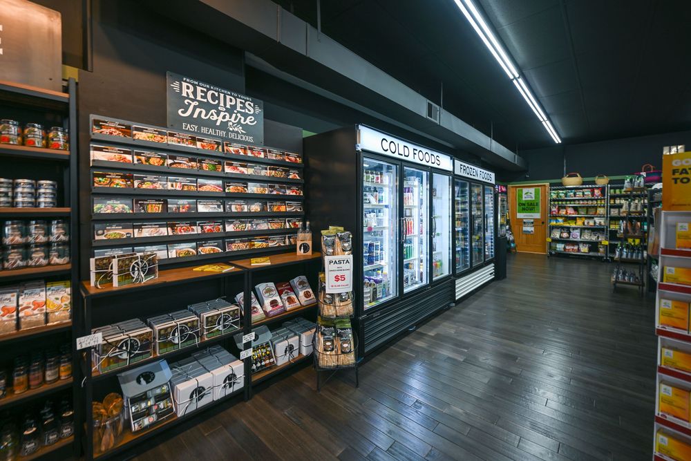 Modern grocery store aisle with recipe inspiration display, refrigerated cold food section, and dark wood flooring.