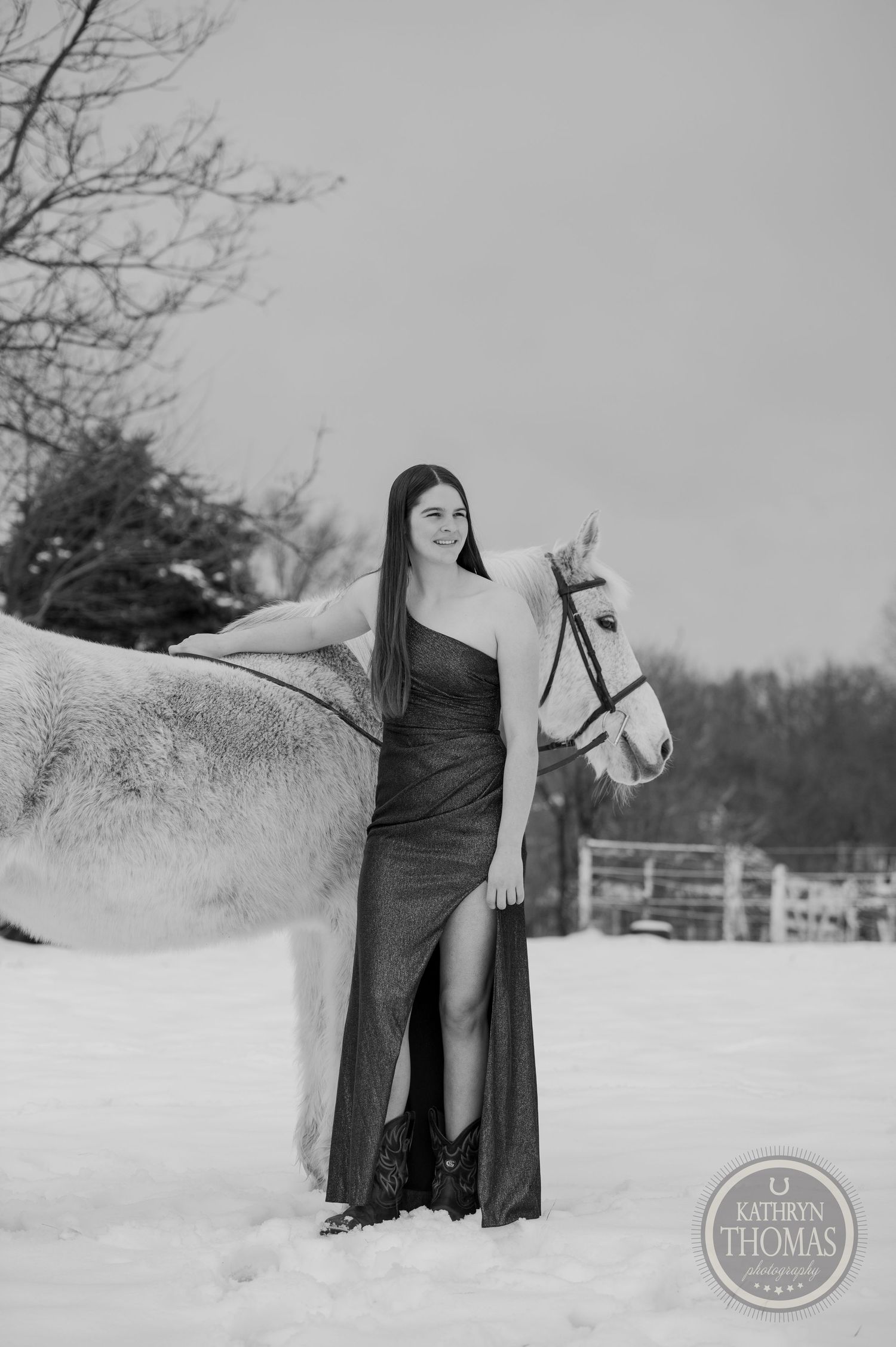 A black and white portrait of a person in a formal dress posing with a white horse in the snow.