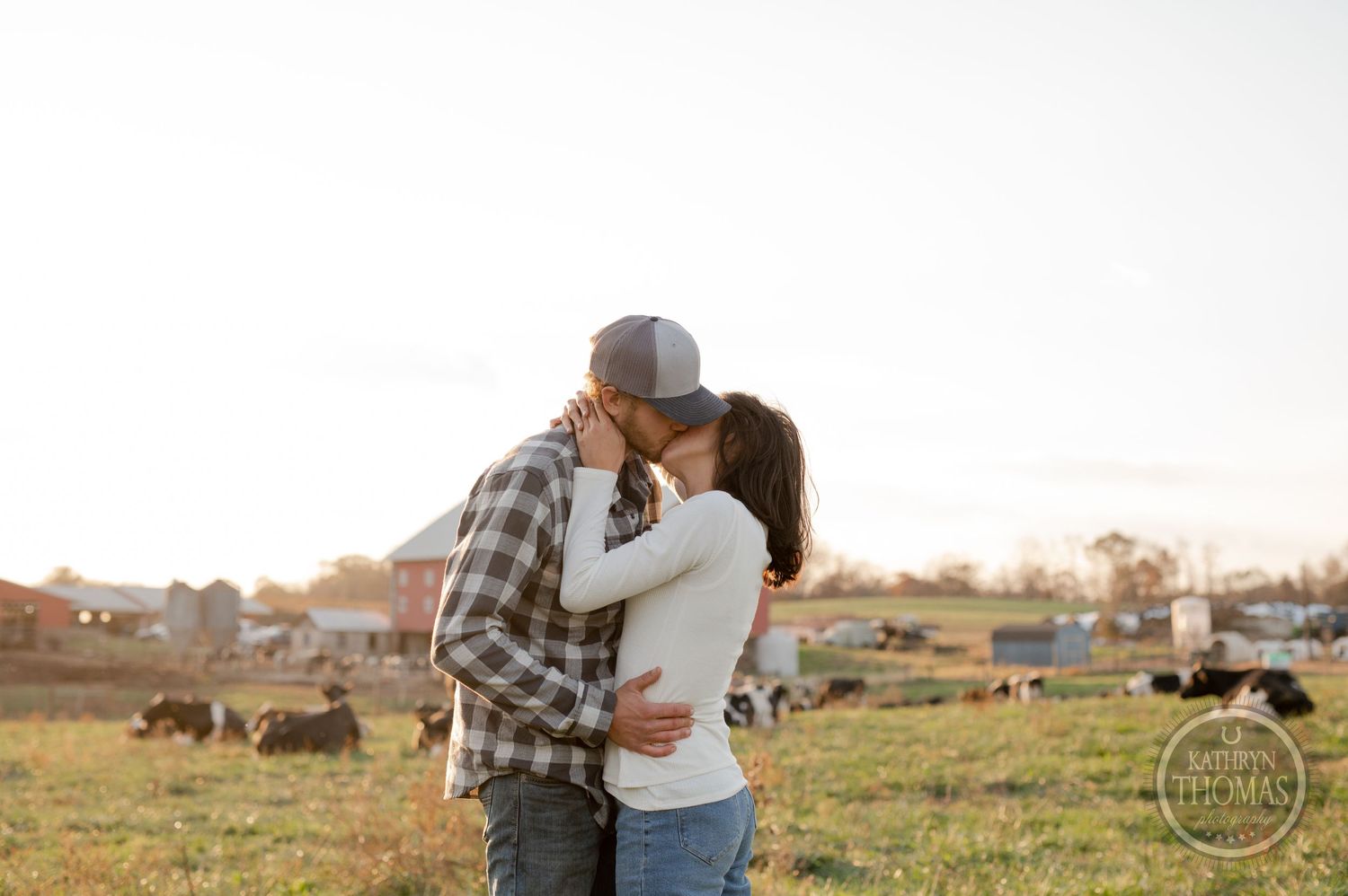 A tender embrace captured against the backdrop of a rustic farm setting at sunset.