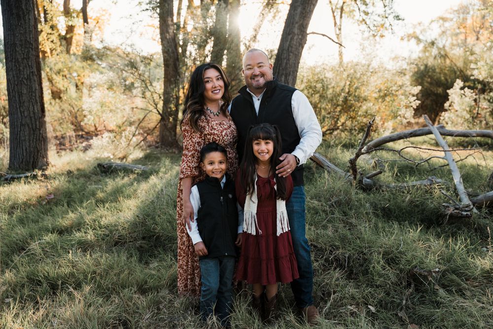 Family group photo session in a sunlit forest with autumn colors and natural lighting.