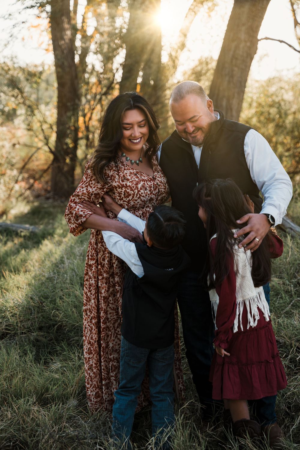 Family sharing candid laughs and embraces during an outdoor photoshoot in the woods.