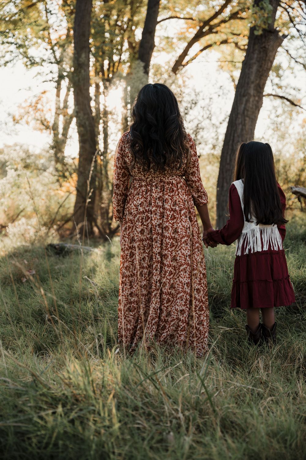 Back view of family members in coordinated burgundy and floral outfits standing in tall grass.