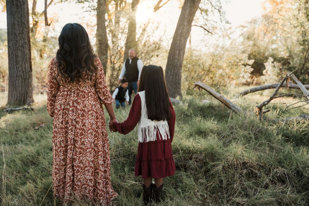 Side view of family members in autumn attire standing in tall grass during golden hour.