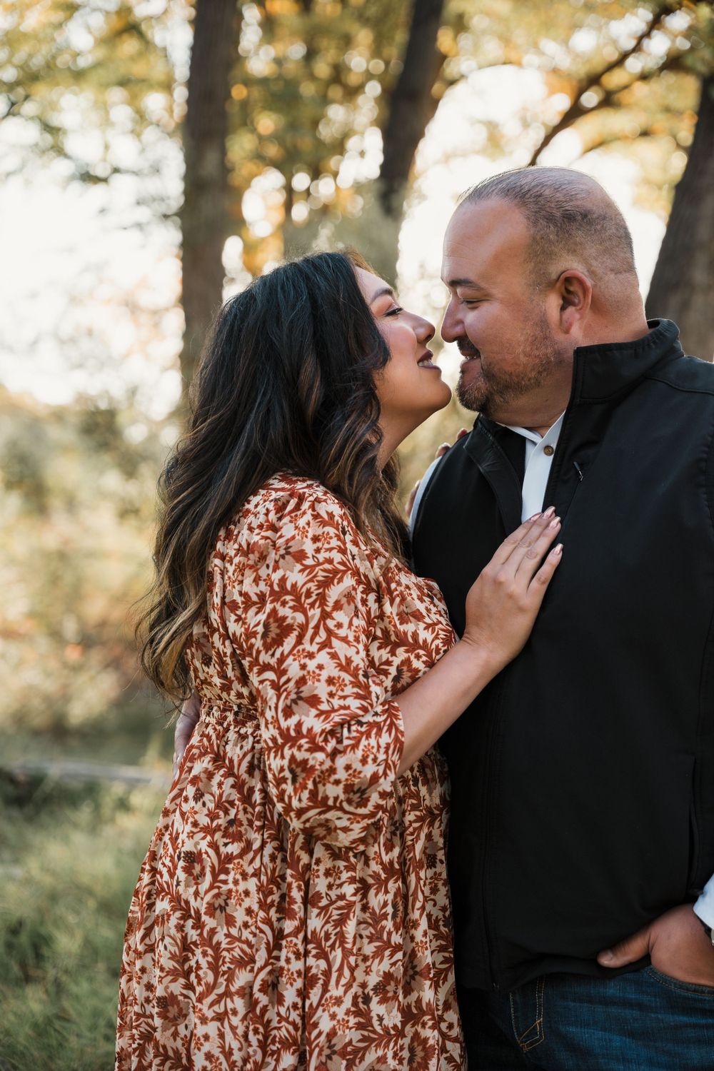 Romantic couple portrait in black and floral attire against natural forest backdrop.