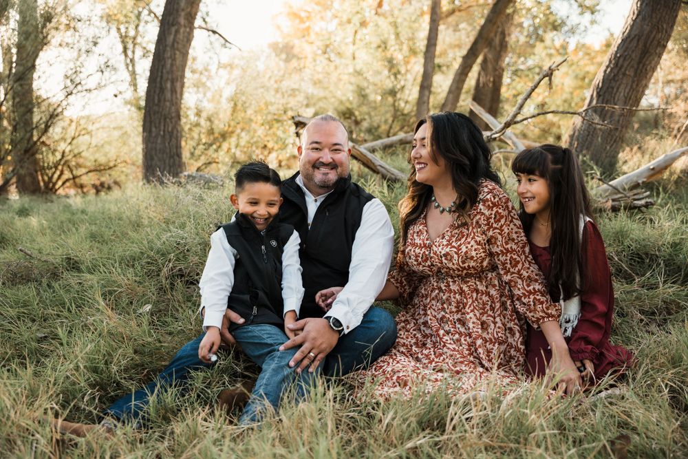 Family poses together on grassy hillside with trees during fall photography session.