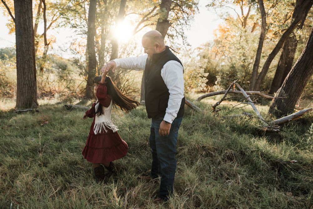 Playful family moment captured in sunlit wooded area during autumn photoshoot.