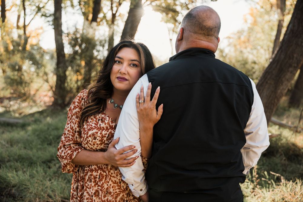Couple embracing in wooded setting during golden hour autumn photoshoot.