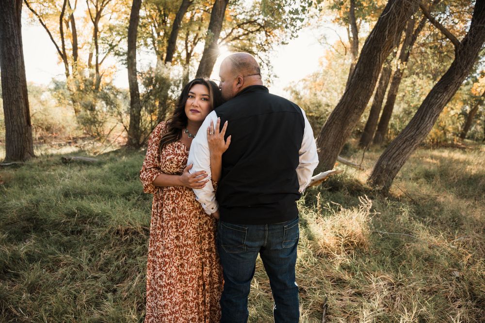 Romantic couple pose together against backdrop of autumn trees during outdoor photo session.