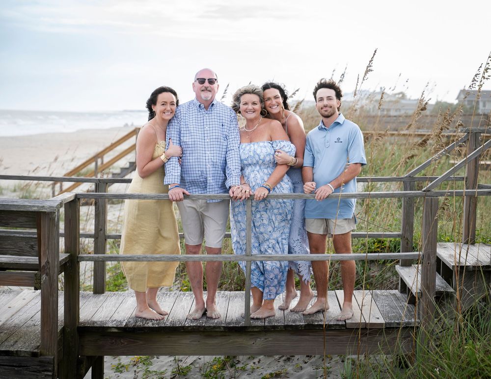 A group of people standing together on a wooden boardwalk at the beach during sunset.