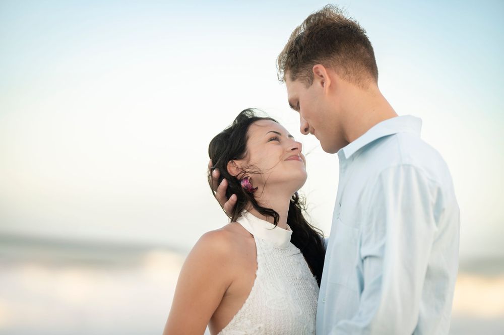 Couple sharing a romantic moment on a beach, smiling at each other in soft natural light.