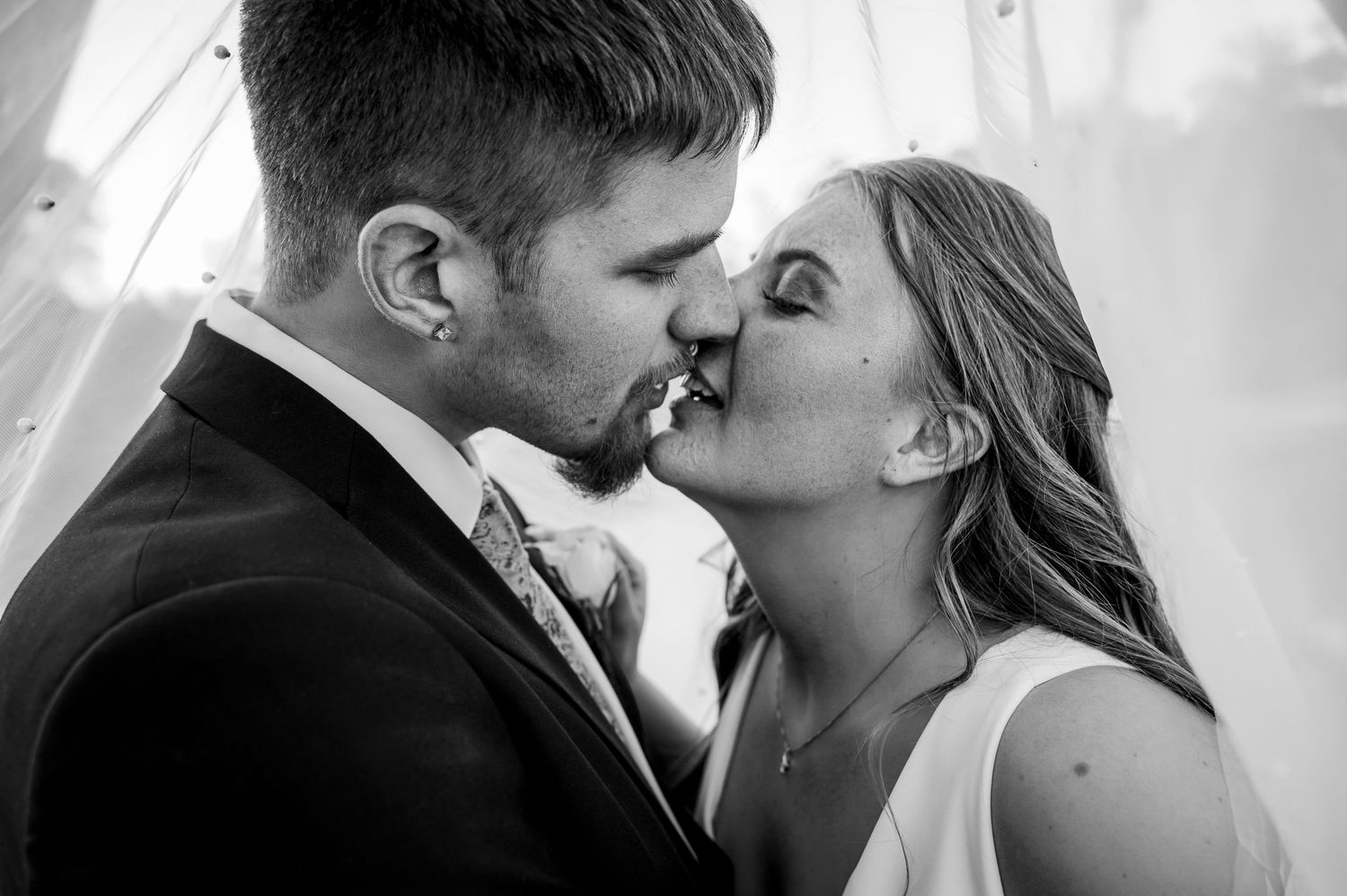 Black and white photo of a bride and groom sharing a romantic kiss at their wedding ceremony.