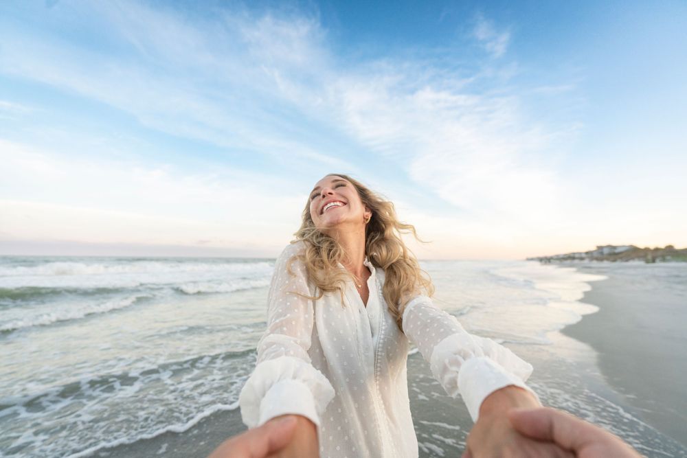 Woman in white dress twirling joyfully on beach at sunset.