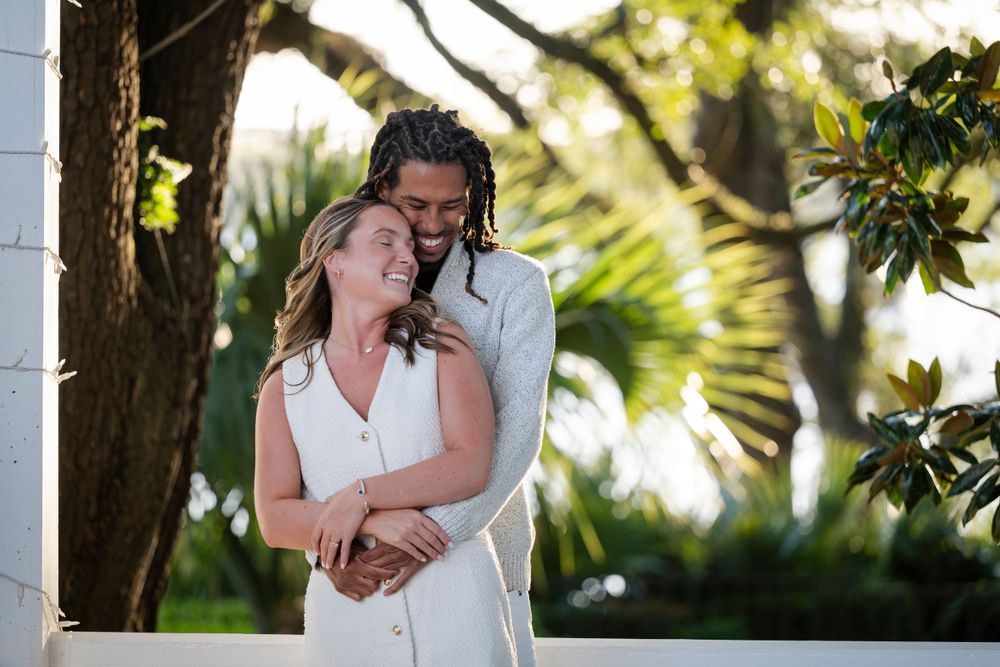 A tender embrace between a couple in white clothing amid lush tropical greenery.