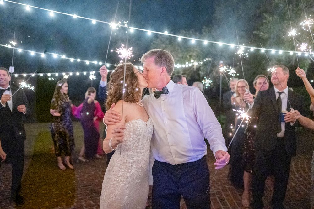 A couple dances under festive string lights at an outdoor evening wedding reception while guests celebrate around them.