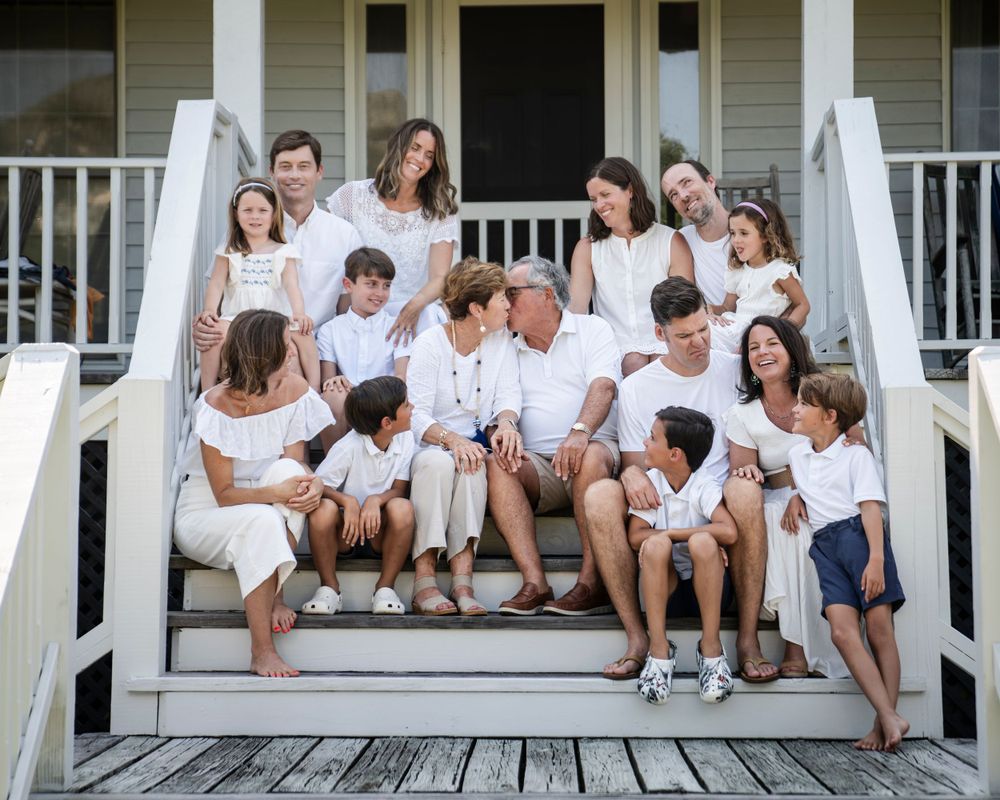 A large family group wearing coordinated white outfits poses together on white porch steps.