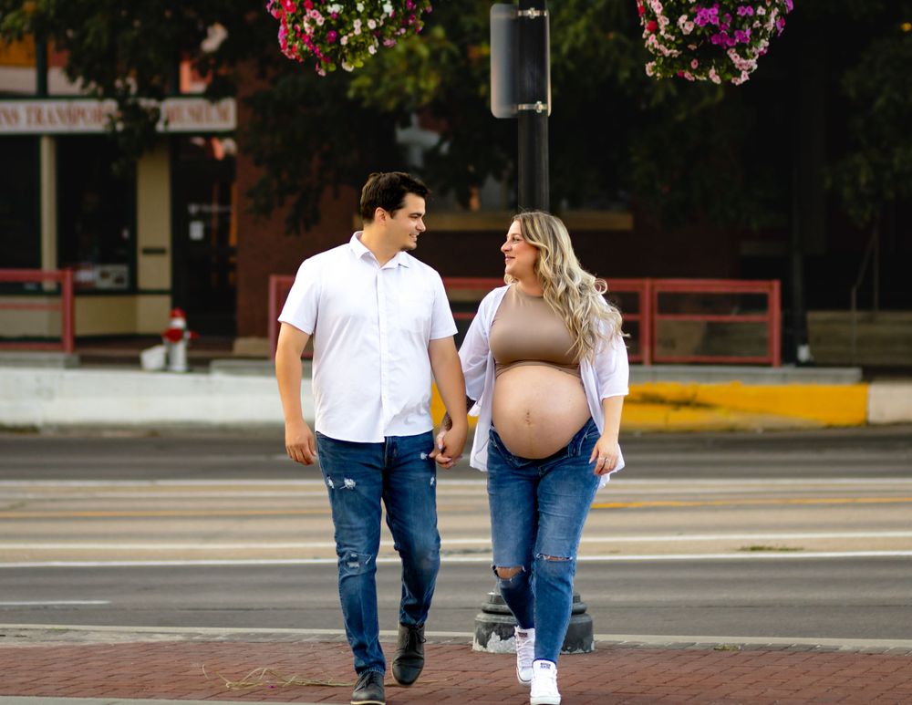Couple walking and holding hands on a crosswalk with pregnant woman in beige top and blue jeans.