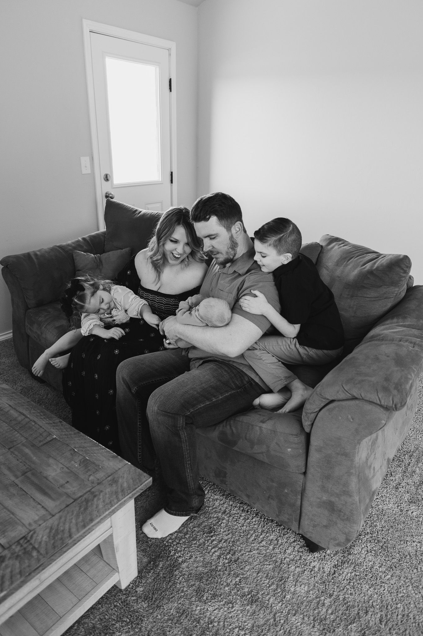 A family sits together on a gray couch reading and bonding in their living room in a black and white photograph.