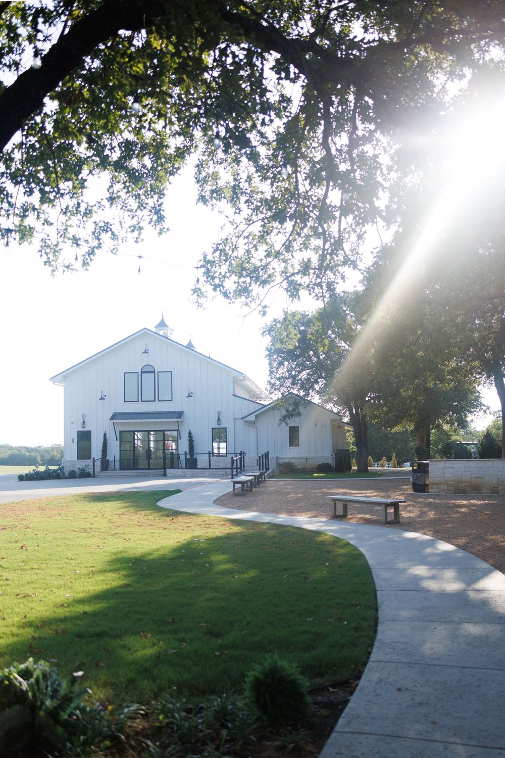 A white church building exterior with concrete walkways and green lawn surrounded by trees on a sunny day.