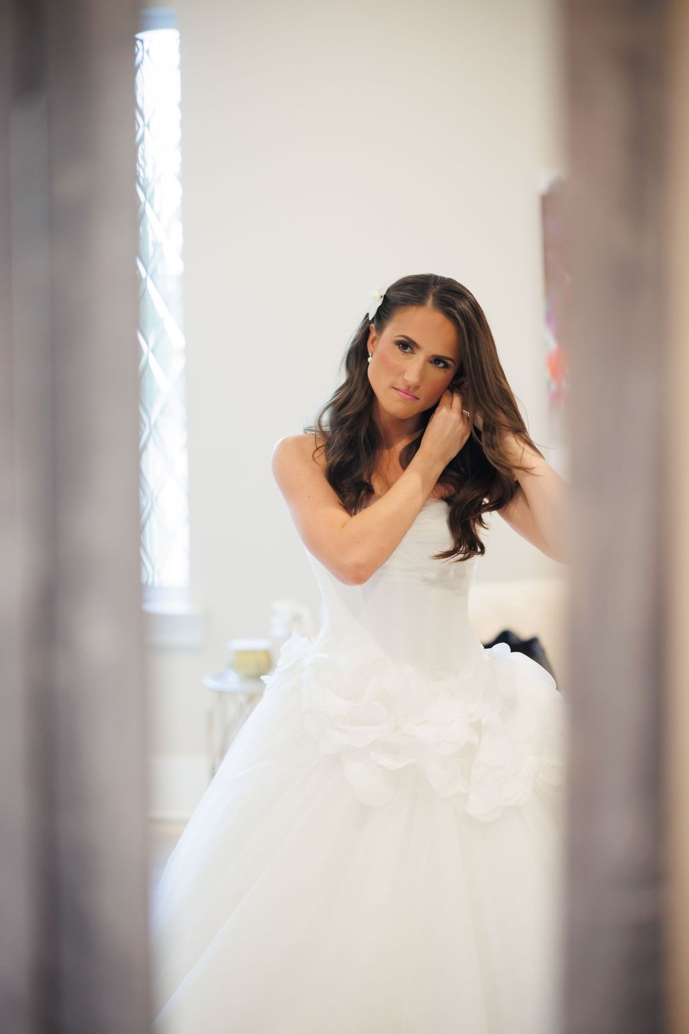A white tulle wedding gown with intricate details photographed in front of a bright window.