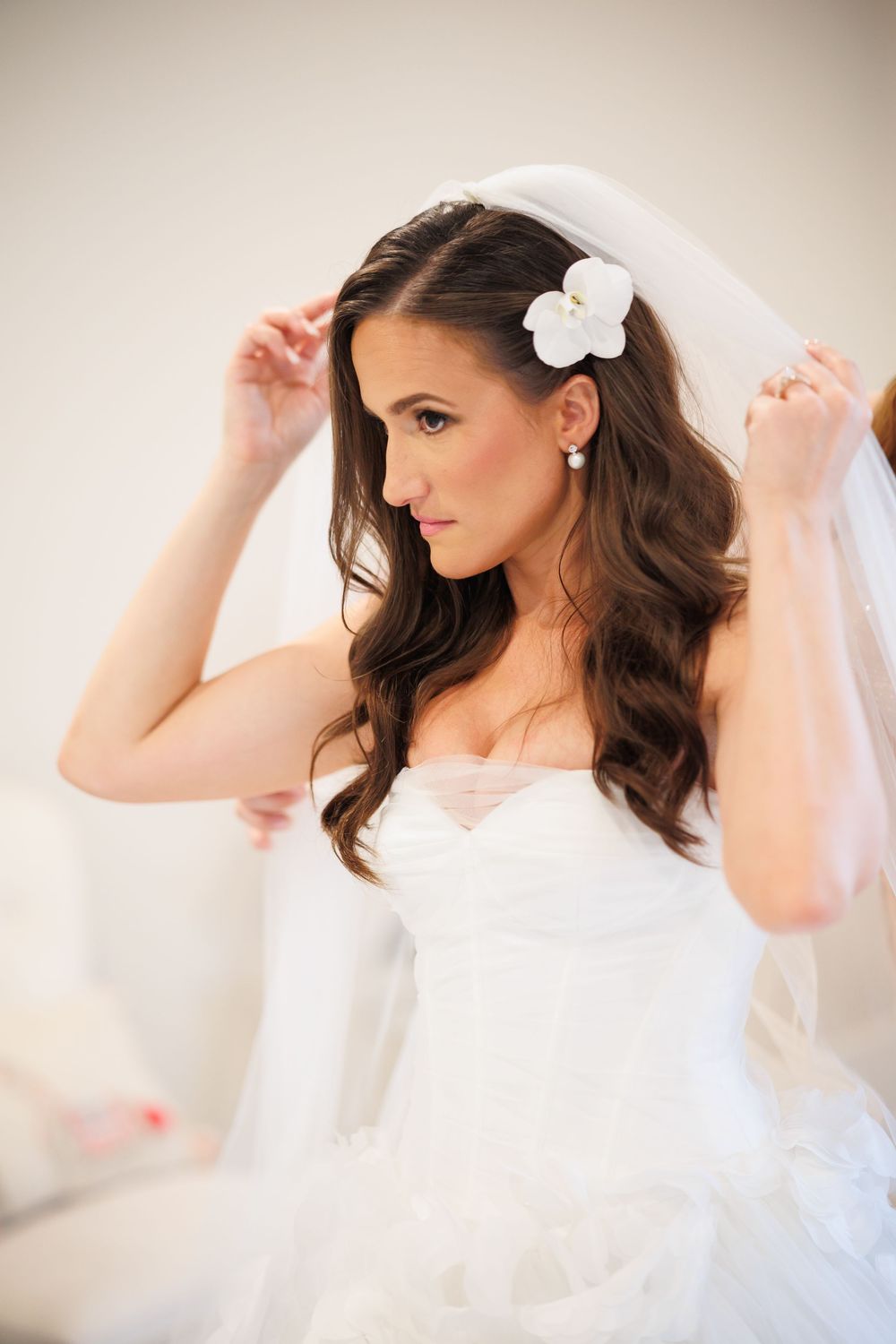 Close-up bridal portraits showing elegant white veil and floral hair accessory against soft beige background.