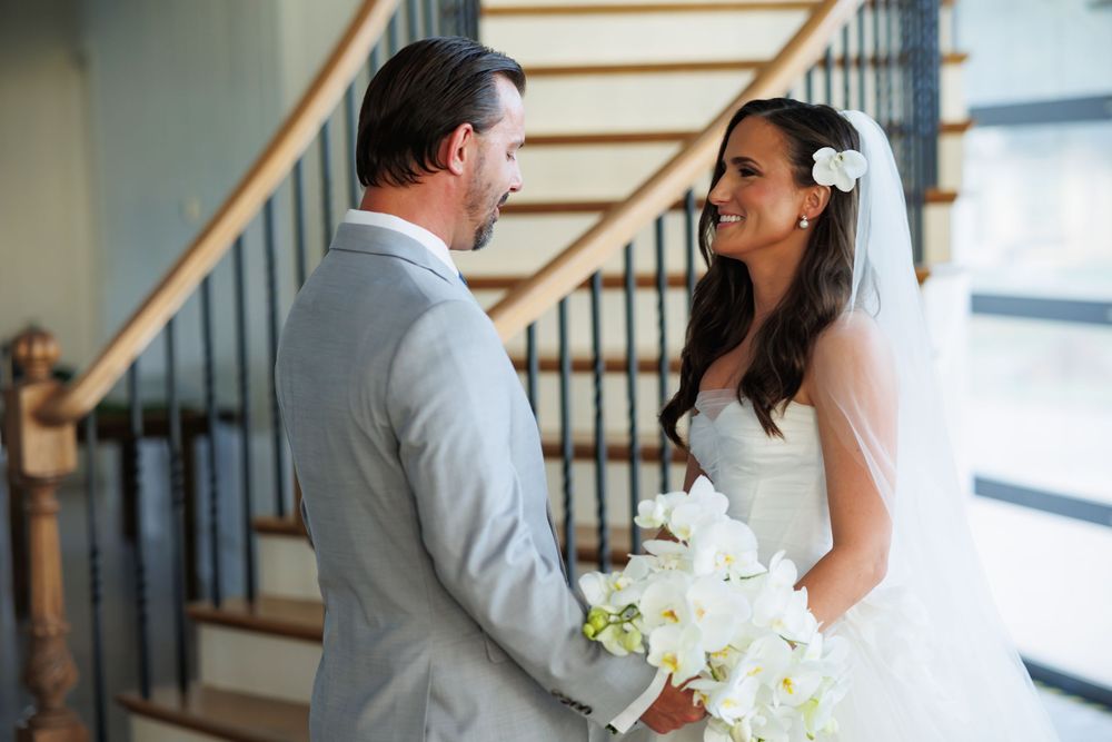 A couple in wedding attire shares a tender moment while holding a white bouquet.