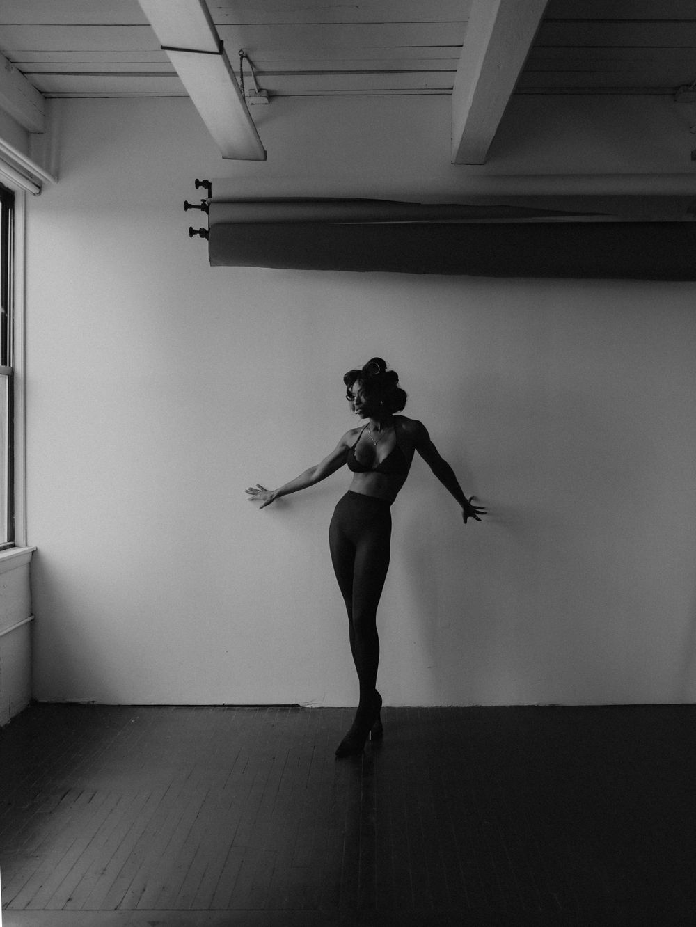 Silhouetted dancer strikes elegant pose against white studio wall.