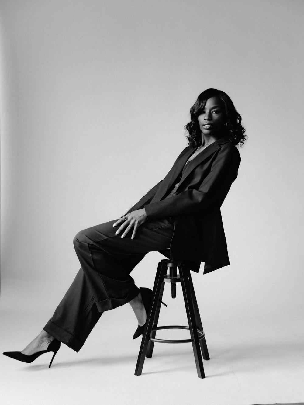 Classic black and white portrait on wooden stool featuring power suit and heels.