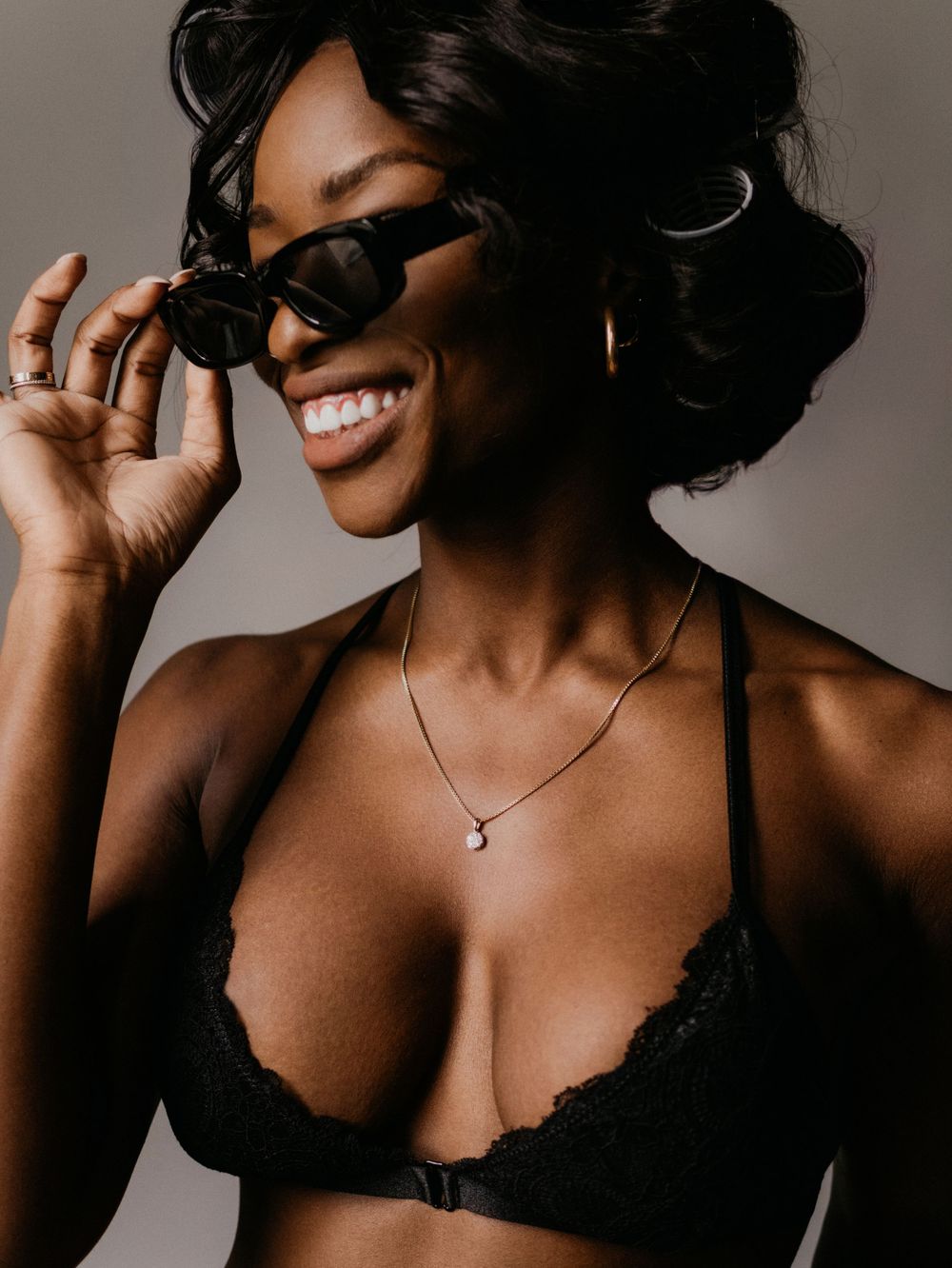 Fashion portrait with sunglasses, black lace bralette and delicate necklace against neutral background.