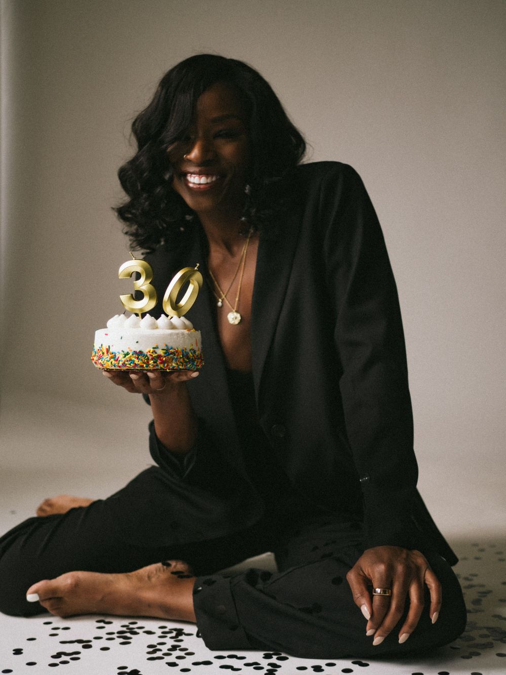 Birthday celebration portrait with model in black outfit holding cake with number 30 candles.