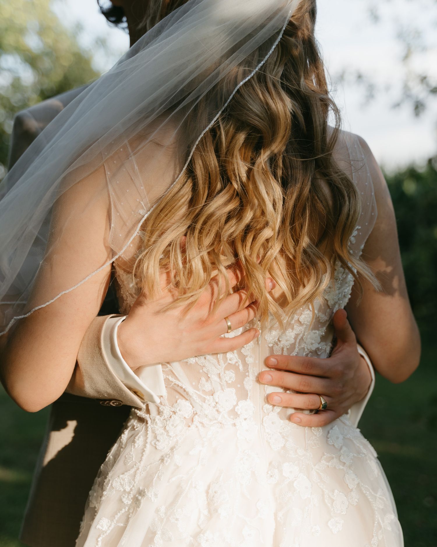 Close-up detail of a bride's lace wedding dress back and flowing veil in golden light.