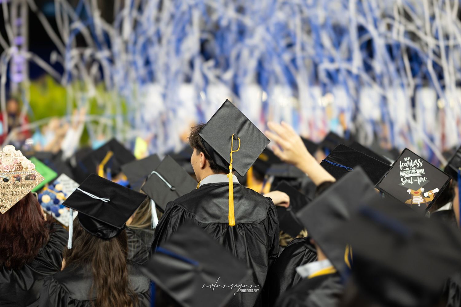 Graduation caps with tassels held high during commencement ceremony with blue and silver decorations.