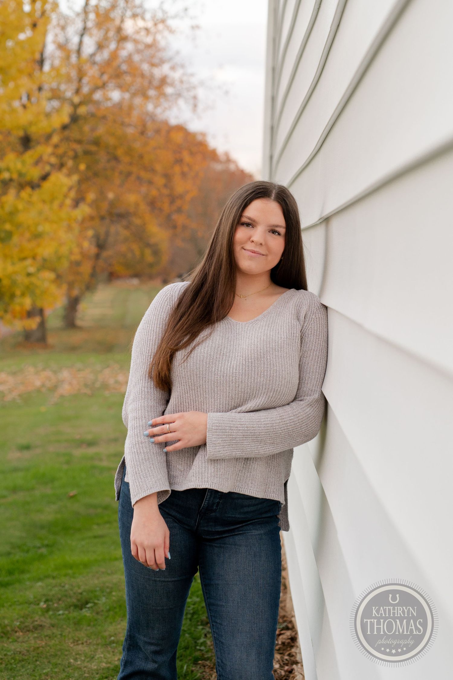 Portrait against white building exterior with golden fall foliage visible.