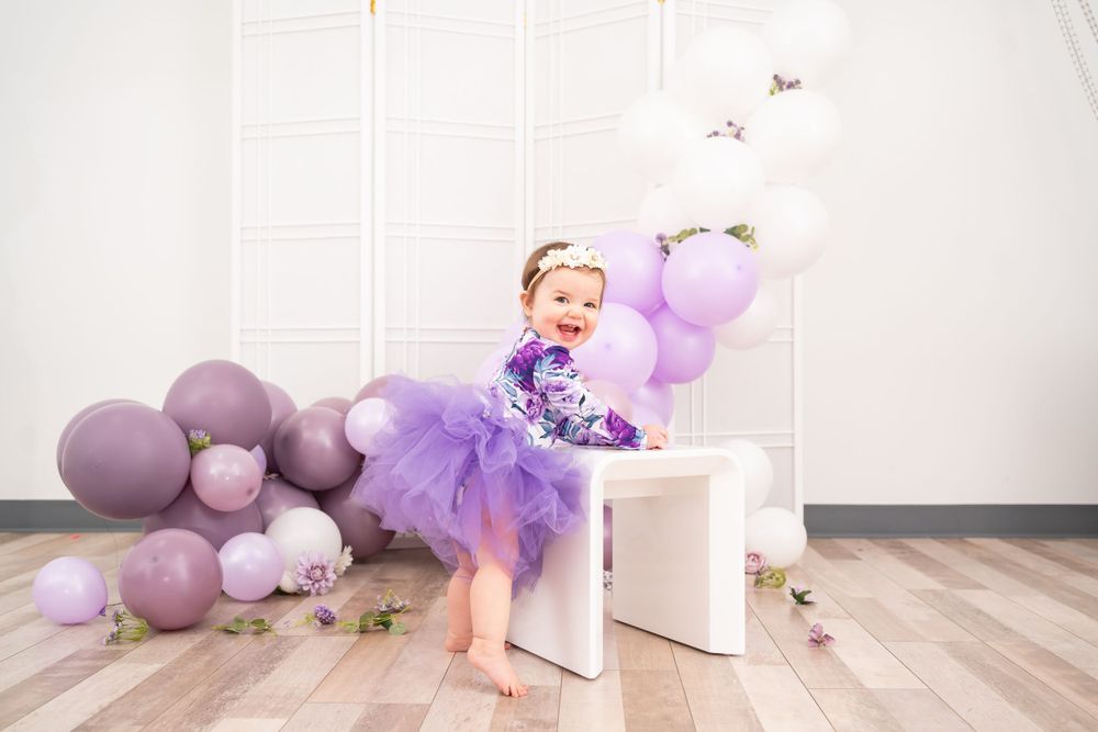 Purple balloon backdrop with white bench and tulle decorations for special occasion photo shoot.