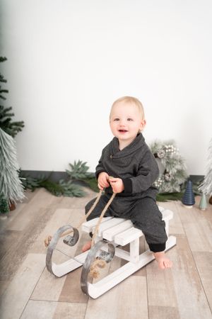 Baby in grey outfit playing with wooden rocking toy on light floor.