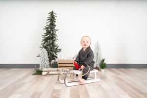 Winter scene with small child on sled surrounded by decorative trees and holiday decor.