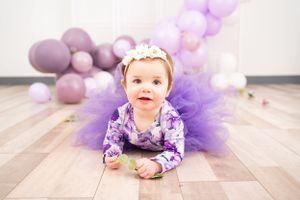 Festive purple balloon and tulle decorations arranged on light wooden flooring.