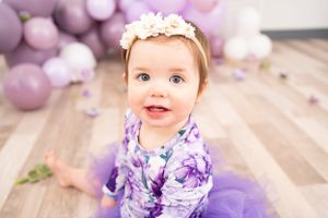 Purple and white themed first birthday party setup with balloons and decorative elements on wooden floor.