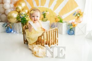 Adorable birthday setup with yellow sunburst backdrop, gold balloons, and blue floral accents.