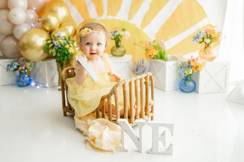 Adorable birthday setup with yellow sunburst backdrop, gold balloons, and blue floral accents.