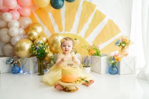 Festive first birthday scene with yellow sun backdrop and balloon arch decorations.