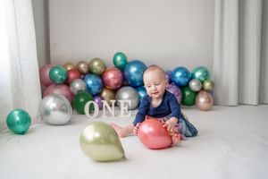 Baby surrounded by colorful balloons at first birthday celebration.