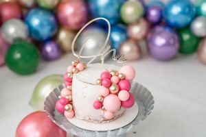 Pink decorated cake with pearl decorations against colorful ornament background.