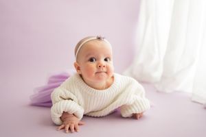Baby in white sweater lying on pink backdrop during studio photoshoot.